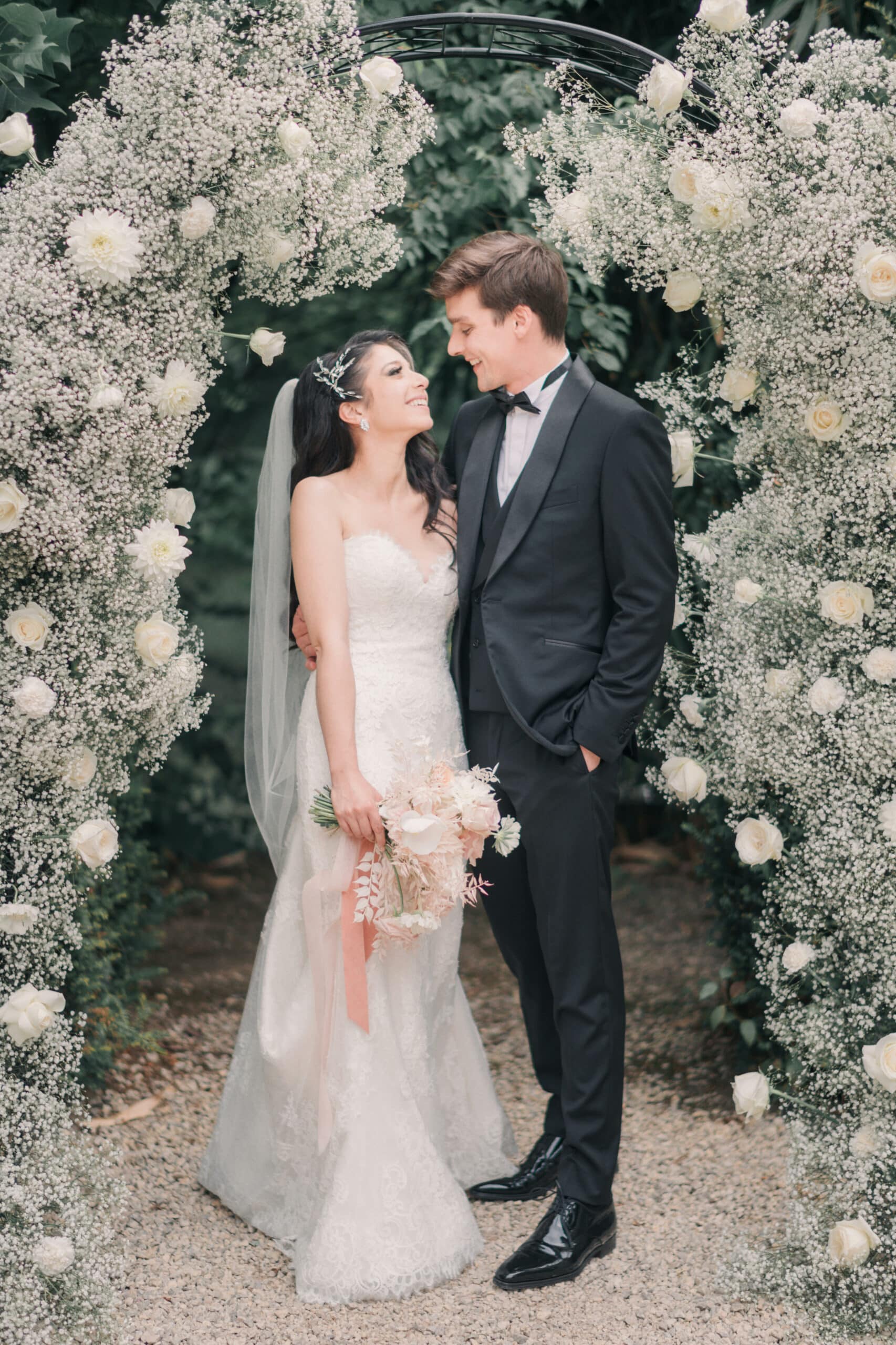 Les mariés devant une arche de fleurs en gypsophile et roses blanches